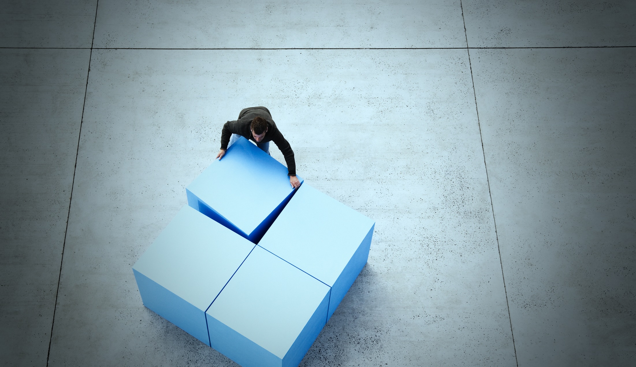 A photo of a businessman, seen from above, shoving four massive cubes together