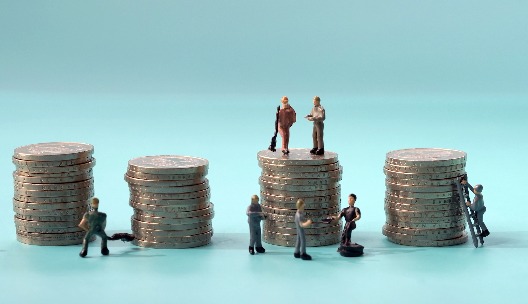 Miniature toy figures of laborers stand beside towers of silver coins.