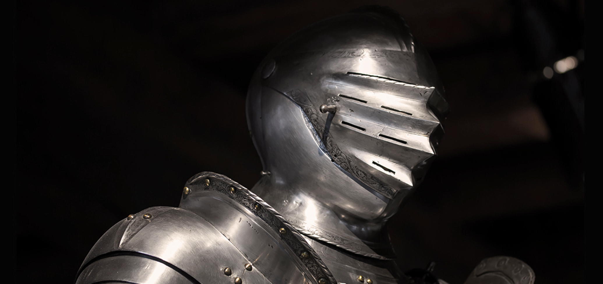 A photo of the head and shoulders of a knight in silver armor with a helmet bearing thin slits over the eyes.