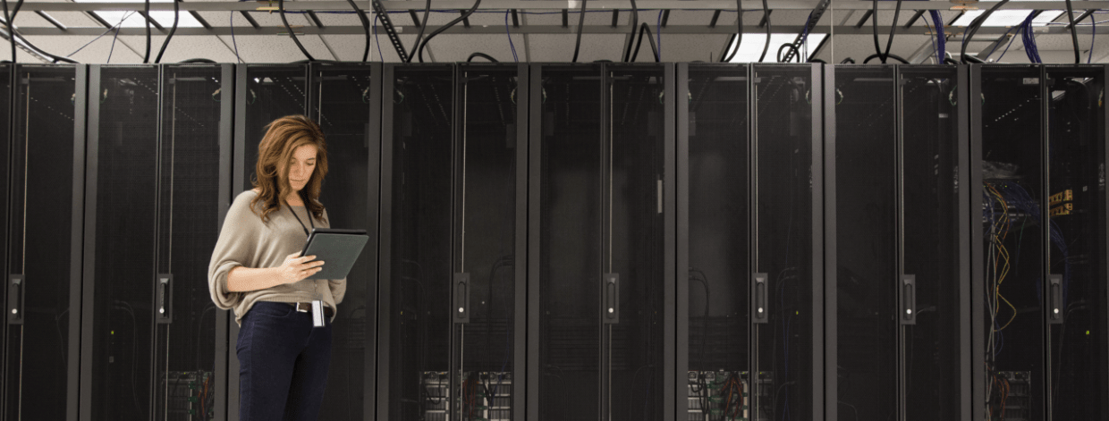 stock image: woman with tablet computer standing in front of a large server stack