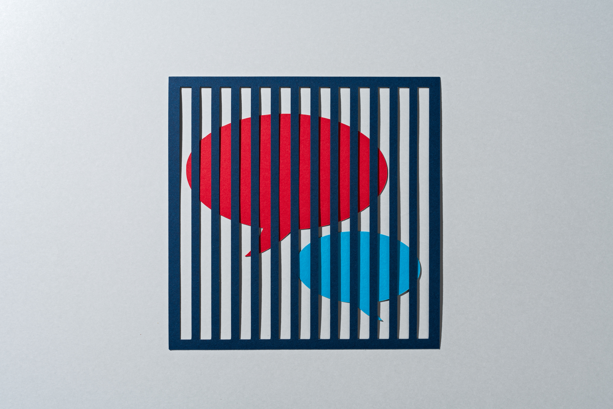 Two speech bubbles, one red, one turquoise, sit caged behind bars.