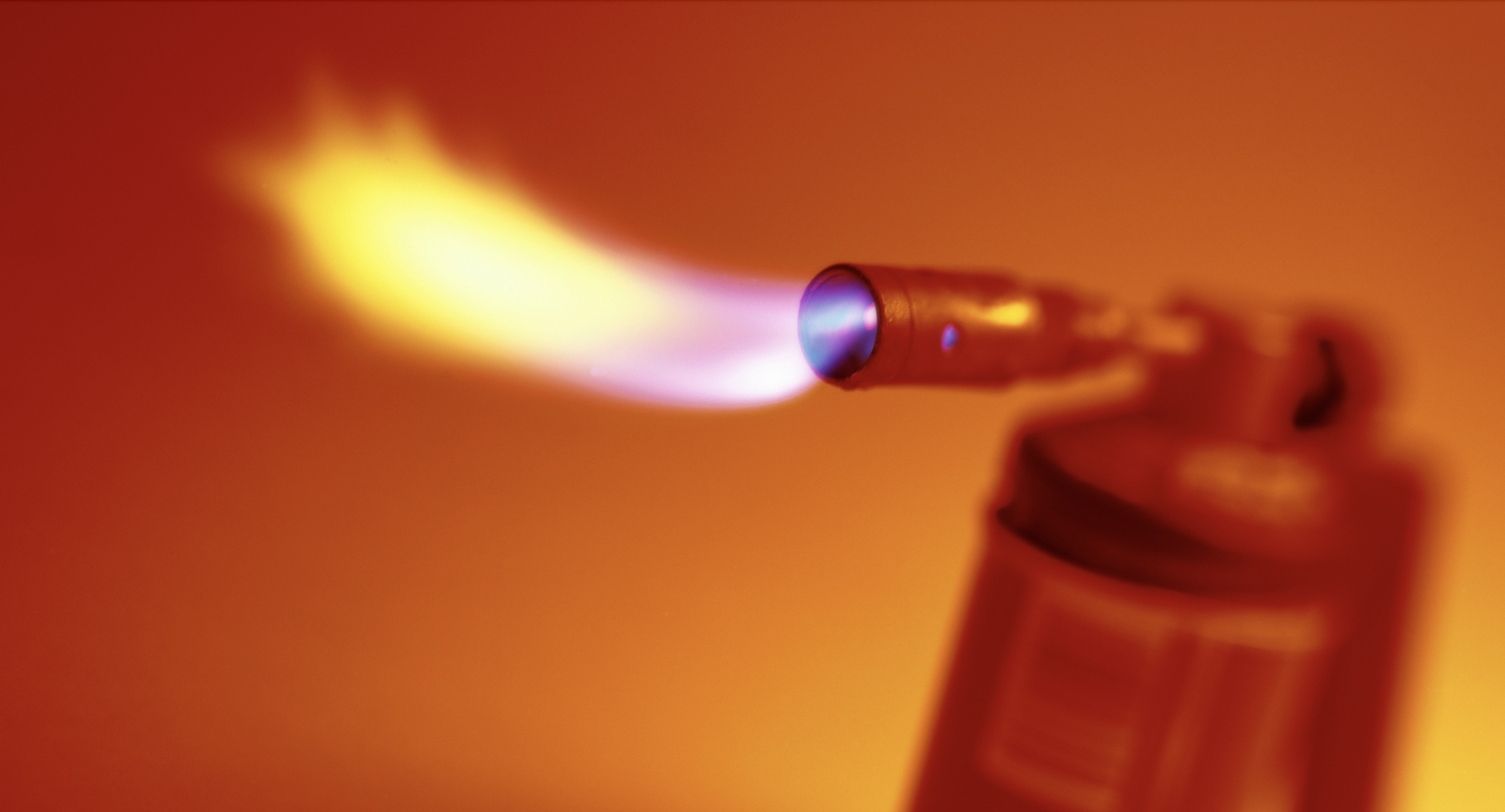 A photo of a red blowtorch spewing flames, and set against an orange backdrop.