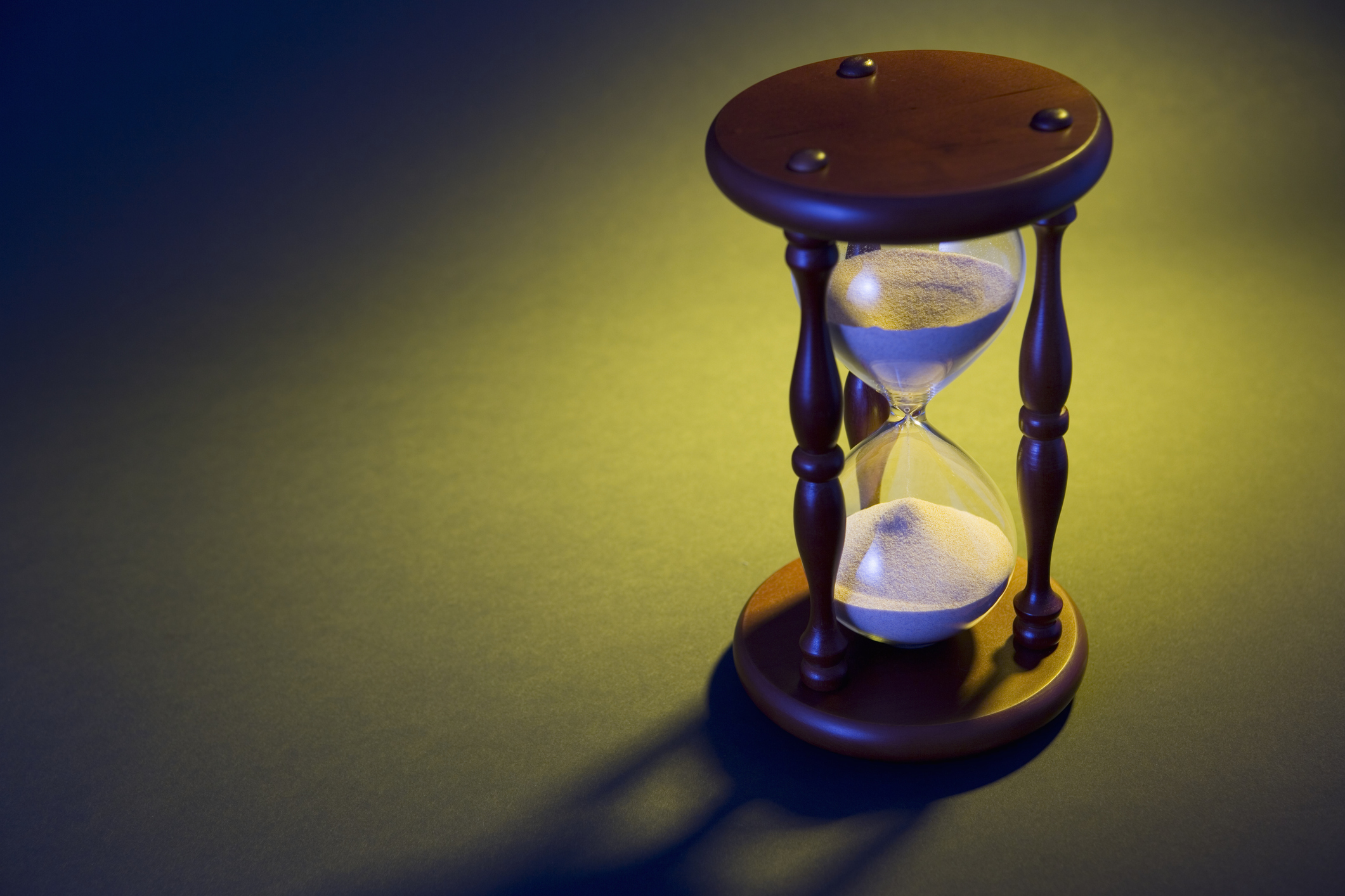 A photo looking down on an hourglass seeping white sand and set against a yellow-ish spotlight.