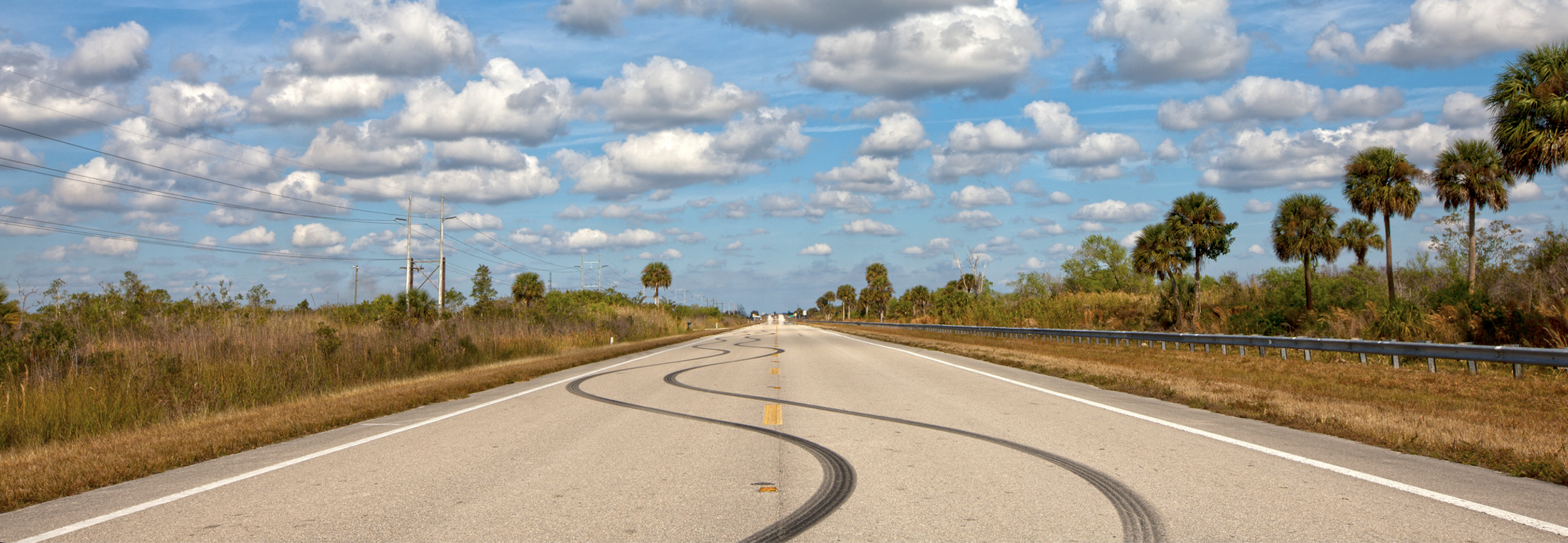 A photo of swerving tire skid marks on a two-lane highway that stretches into the distance.