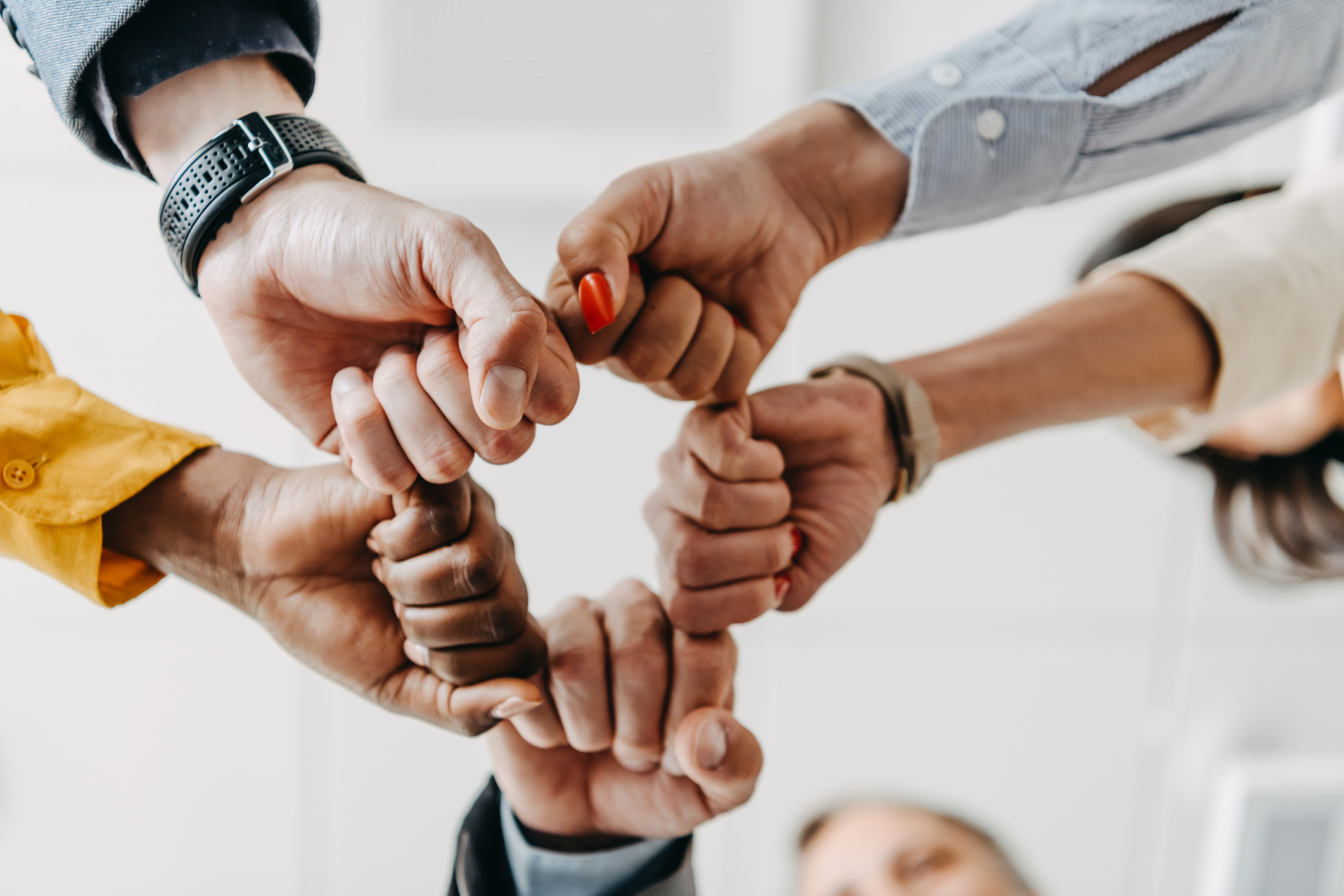 A cluster of five multiethnic office workers doing a group fist bump