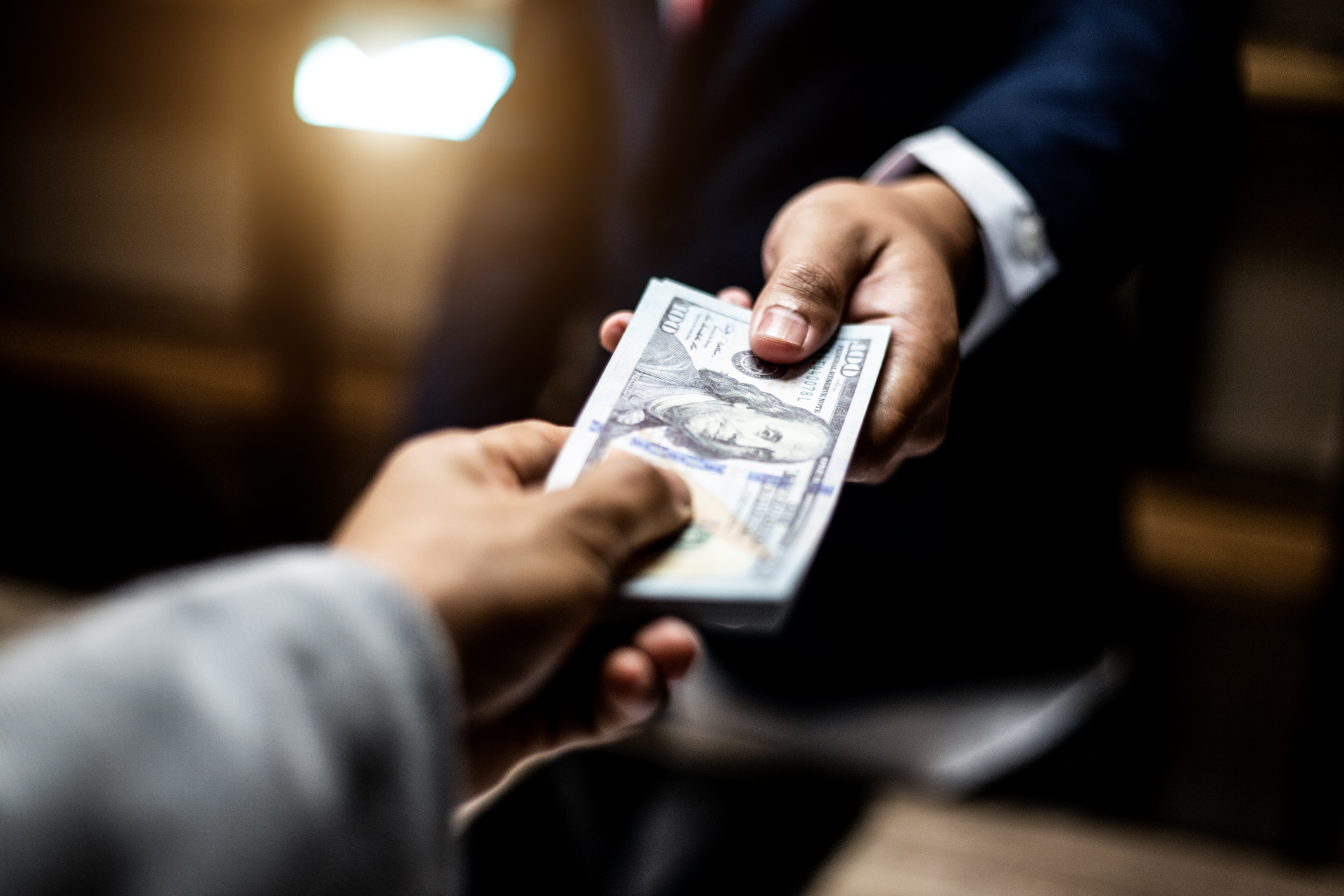 Photo of a hand passing a wad of cash to another hand.