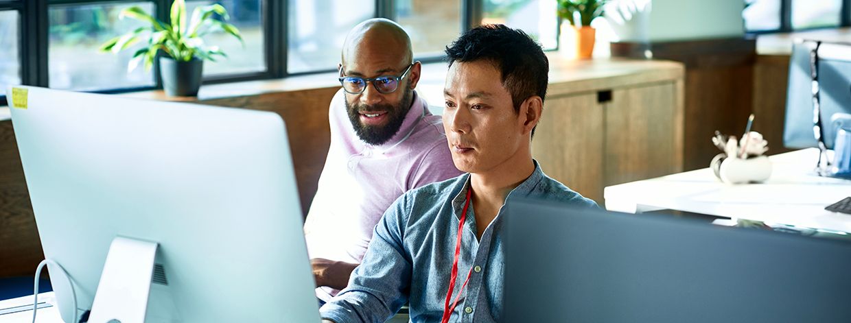 Man sitting at desk using computer, IT supporter assisting office worker, software developer looking at screen and concentrating.